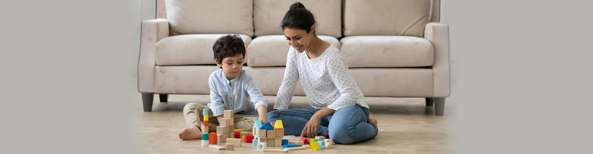 mom helping preschool son to build toy towers from wooden construction blocks